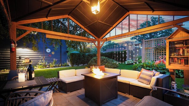 Eine Terrasse im Freien mit Feuerstelle, Korbmöbeln und einem Bücherregal.