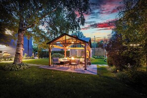 Un patio al aire libre con una pérgola de madera, mobiliario para sentarse y una chimenea.