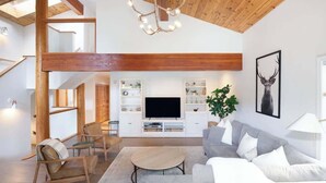 Un soggiorno spazioso con soffitto alto, travi in legno, televisione a schermo piatto e una pianta grande.