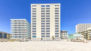 Hotel de vários andares com varandas, situado numa praia arenosa.