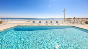 Piscina azul límpida com vista para o oceano, uma bandeira e uma área cercada com espreguiçadeiras.