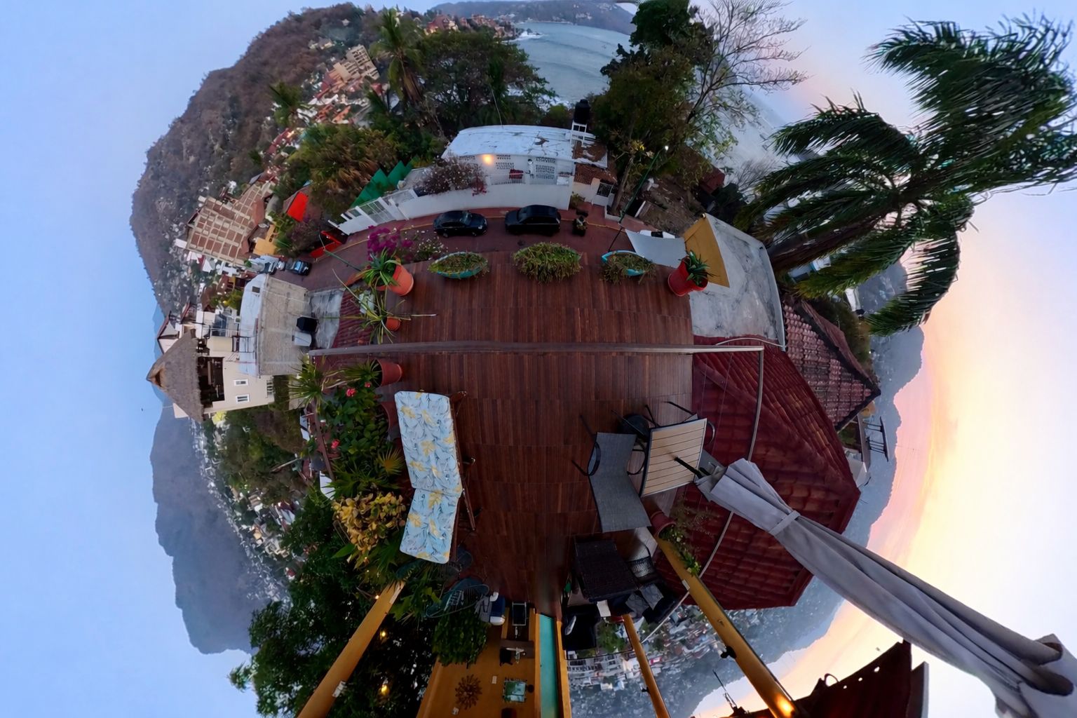 Panoramablick von einer Dachterrasse mit Außenmöbeln, umgeben von üppigem Grün und mit Blick auf eine Küstenlandschaft.