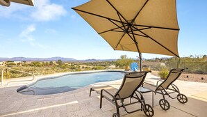 Zona de piscina amb vistes a les muntanyes, dues gandules i un parasol gran.
