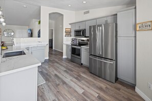 A modern kitchen with stainless steel appliances, a white countertop, and a wooden floor.