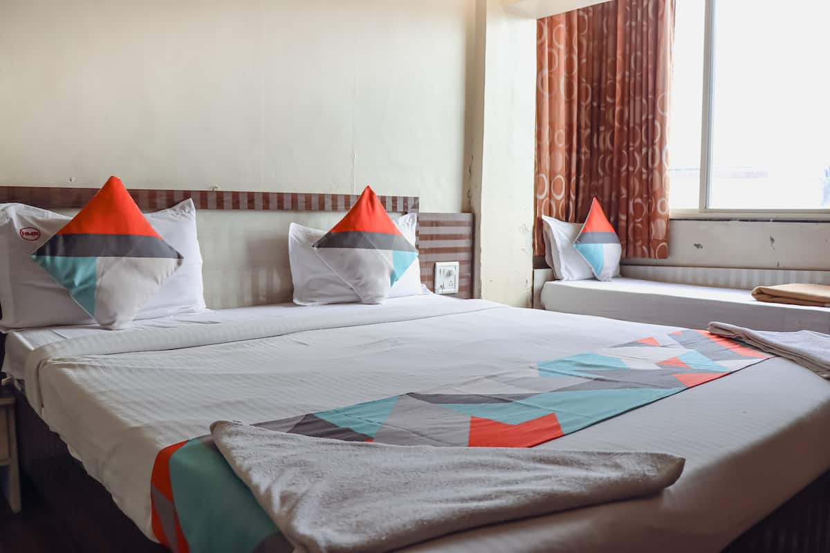 A hotel room with a bed, pillows, a window with curtains, and a bedside table.