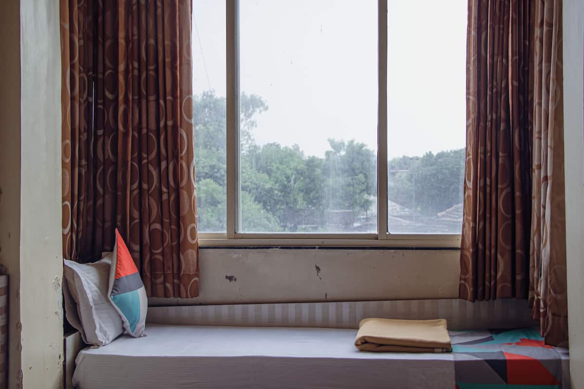A room with a window, a bed with pillows, and a view of trees outside.
