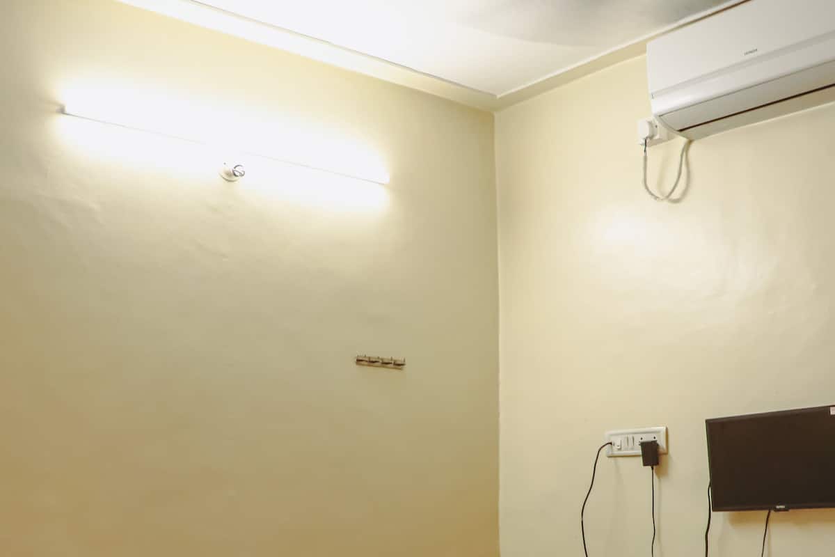 A hotel room with a bed, a ceiling fan, an air conditioning unit, and a wall-mounted TV.