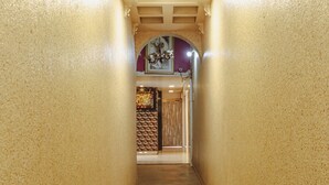 A hallway with a textured wall, a tiled floor with orange diamond patterns, and a ceiling with recessed lighting. - Hotel Mukesh residency (Pune)