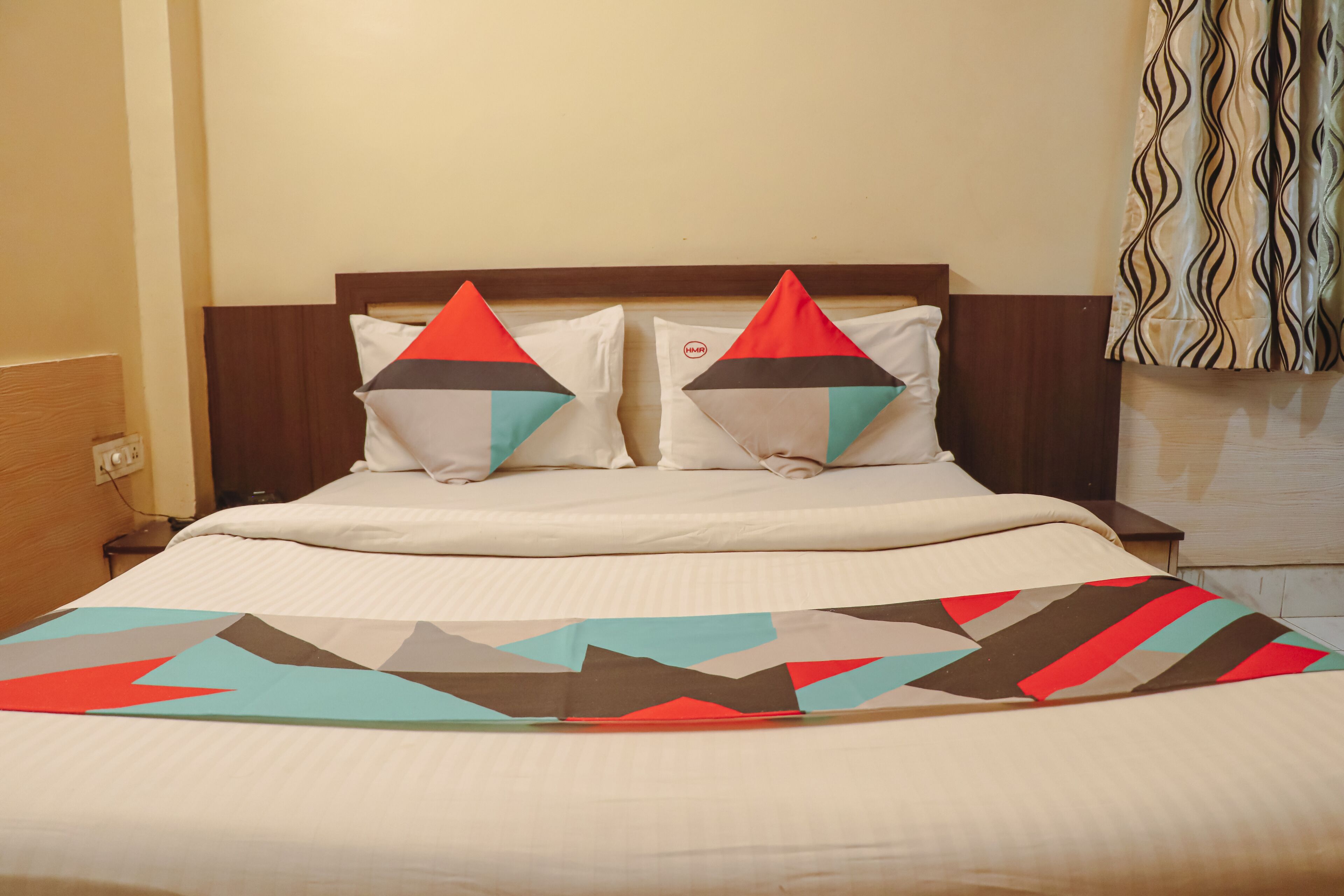 A bed with a patterned bedspread, two pillows with geometric designs, and a wooden headboard.