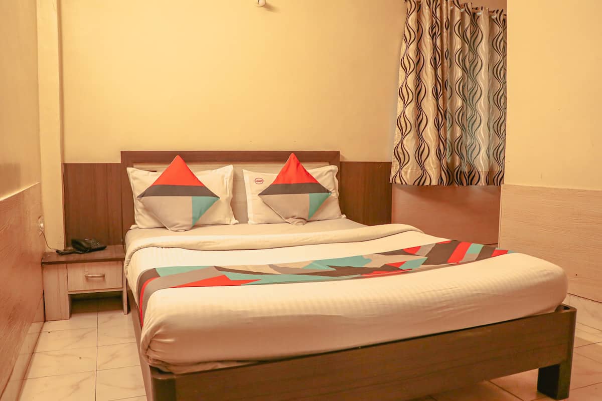A bed with a geometric-patterned bedspread, a wooden headboard, and a nightstand with a phone.
