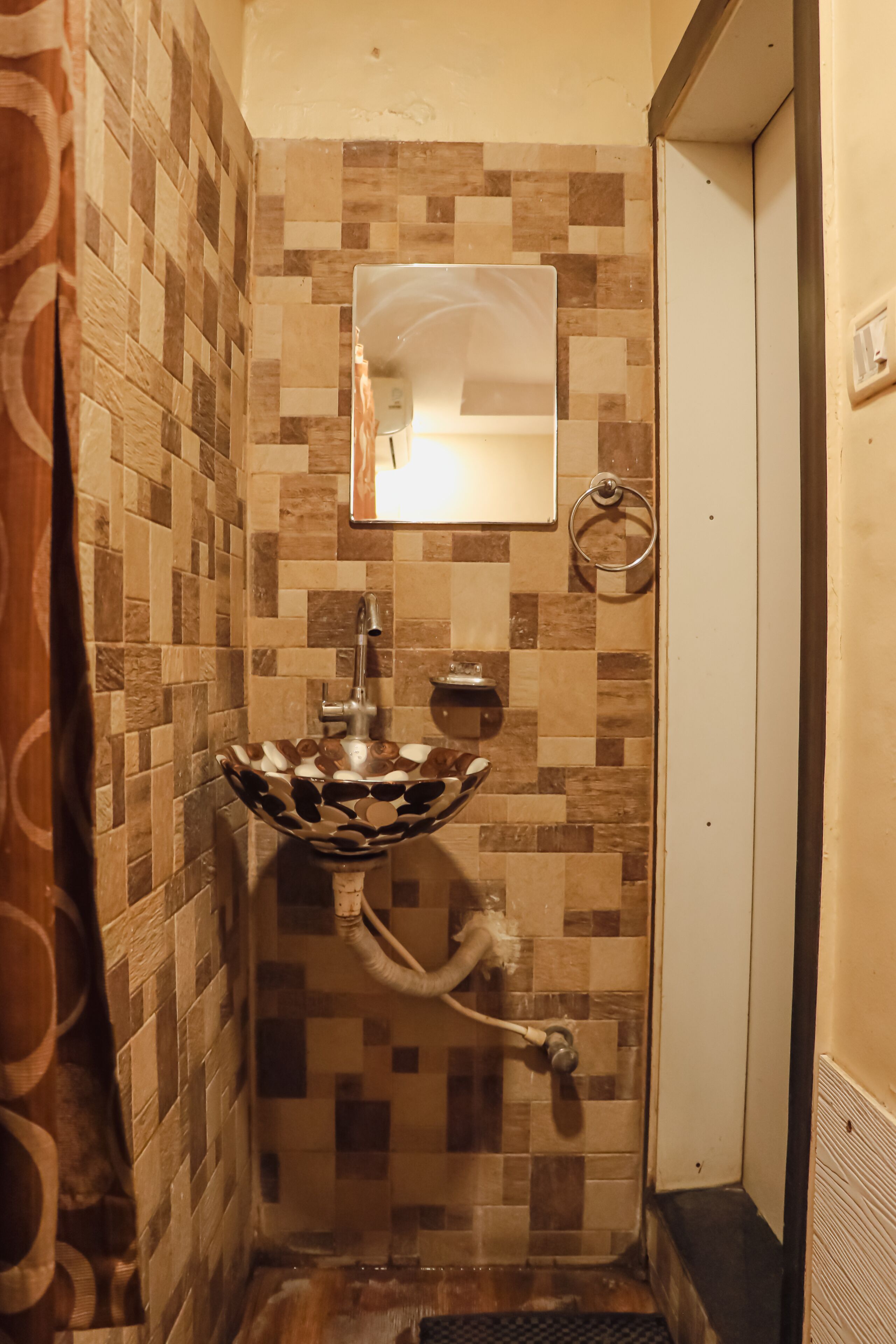 Un bagno con parete rivestita in piastrelle, lavabo con lavatoio decorativo, uno specchio e un porta asciugamani.