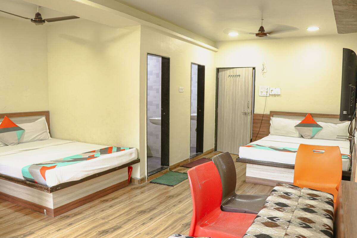 A hotel room with two beds, a red chair, a small table, and a ceiling fan.