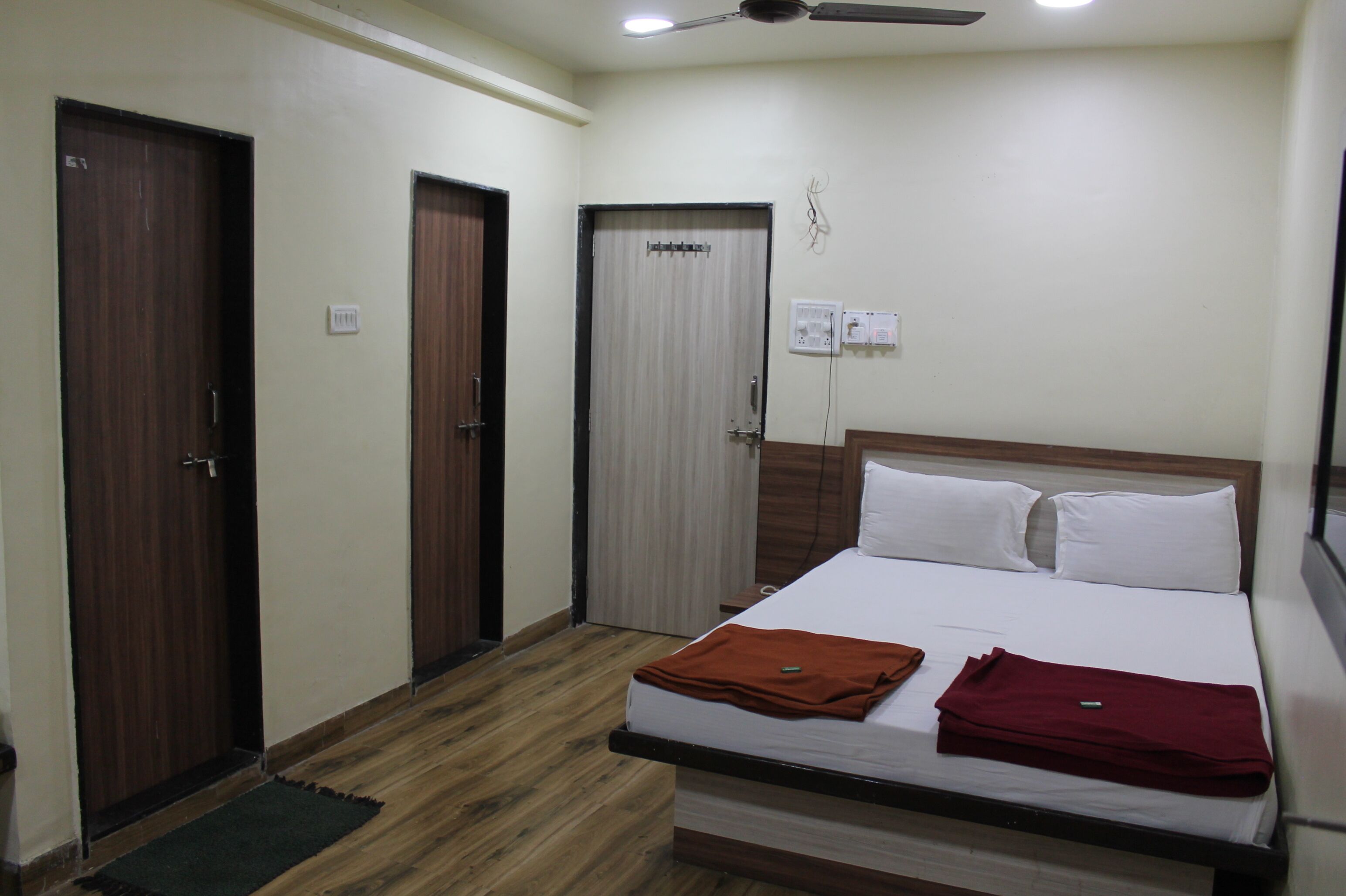 A hotel room with a bed, two doors, a ceiling fan, and a small nightstand.