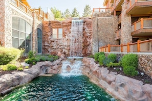 A hotel with a waterfall feature, a pool, and a stone facade.