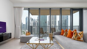 A modern living room with a sofa, ottoman, and coffee table, a TV, and a balcony with a city view. - Dream Inn Apartment- Boulevard Heights (Dubai)