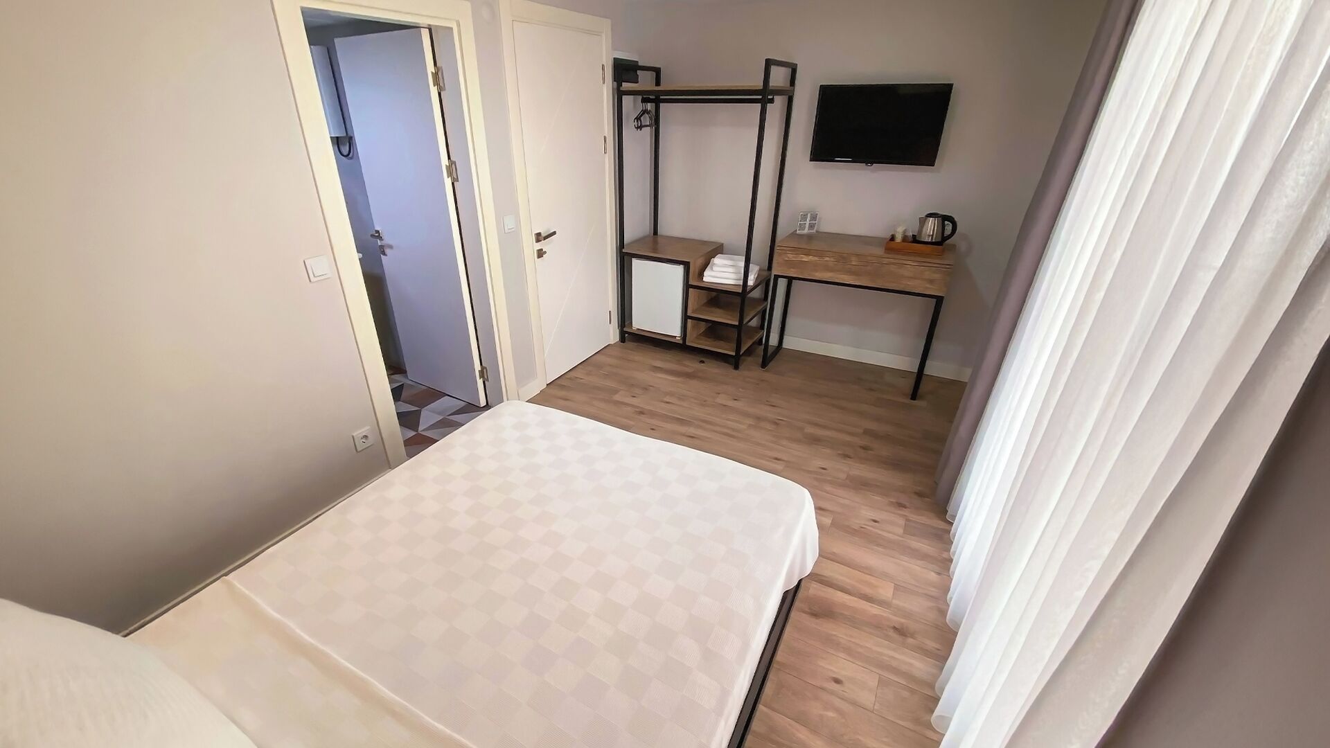 Een kleine hotelkamer met een bed, een bureau, een televisie en een klein kastje.