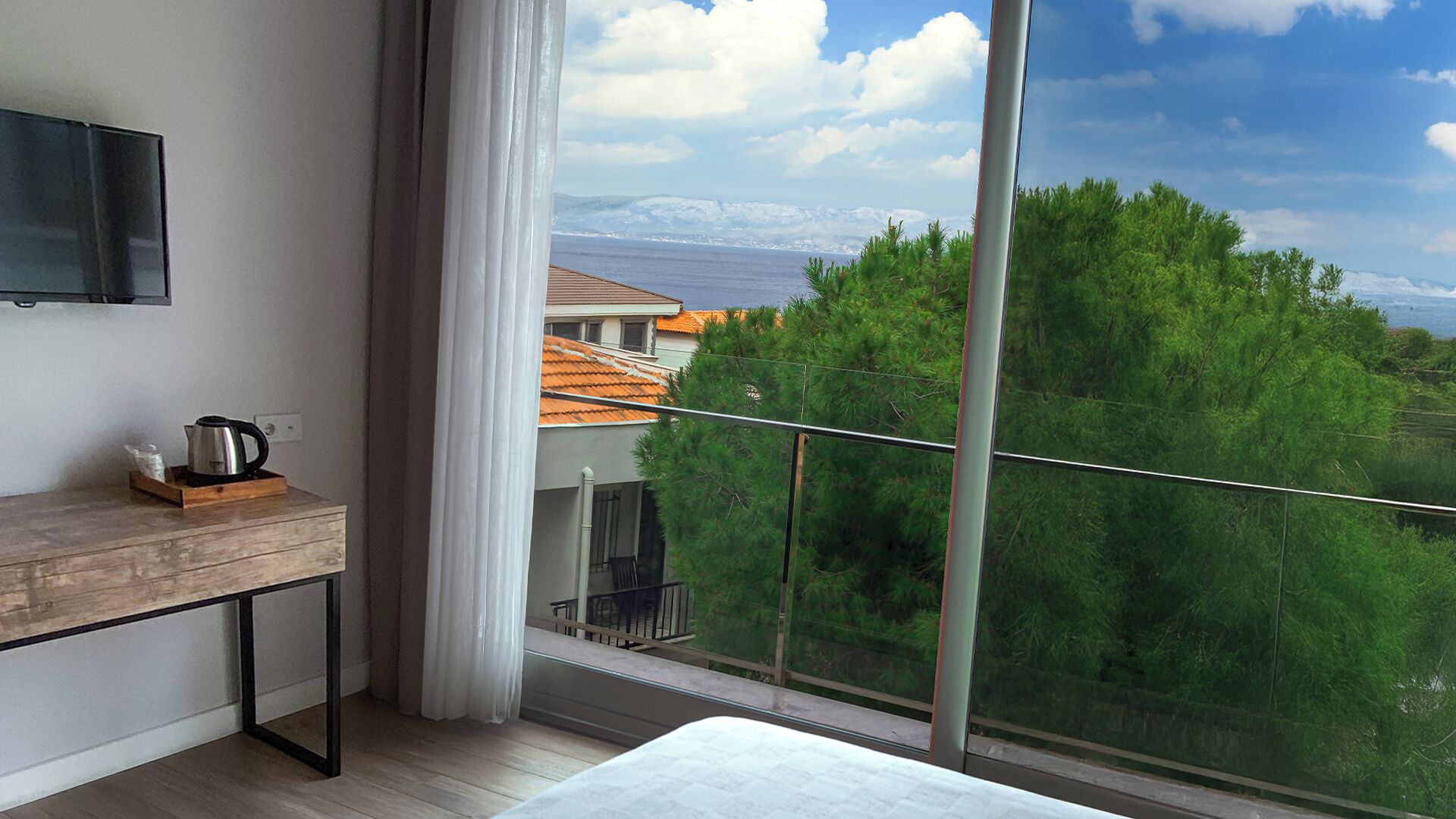 Una habitación moderna con un gran ventanal, un escritorio de madera, un televisor montado en la pared y vistas a un paisaje montañoso.