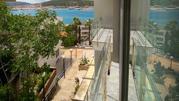 A high-rise building with a glass balcony overlooking a coastal area with boats and a hilly landscape. - Sahil Otel (Cesme)