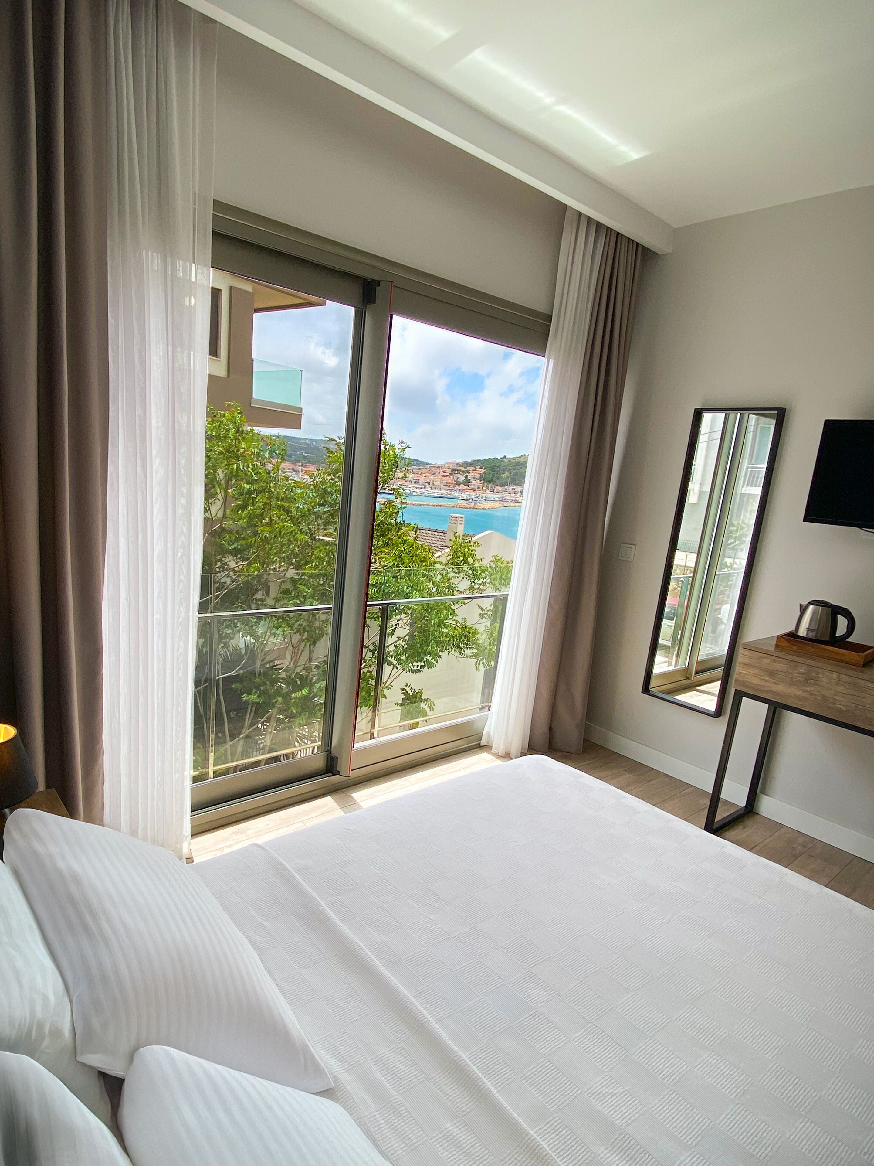 Habitación de hotel con una cama grande, un televisor, un espejo y vistas a la costa.