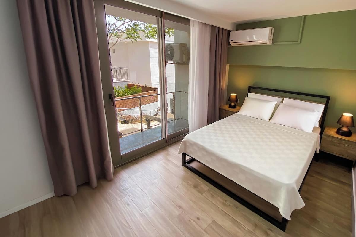 A bedroom with a bed, a nightstand, an air conditioning unit, and a view of the outside.