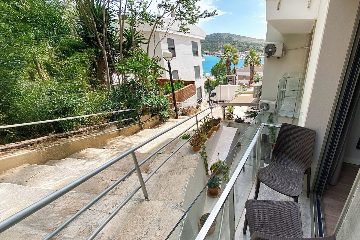 A balcony with a view of a coastal town, outdoor seating, and potted plants.