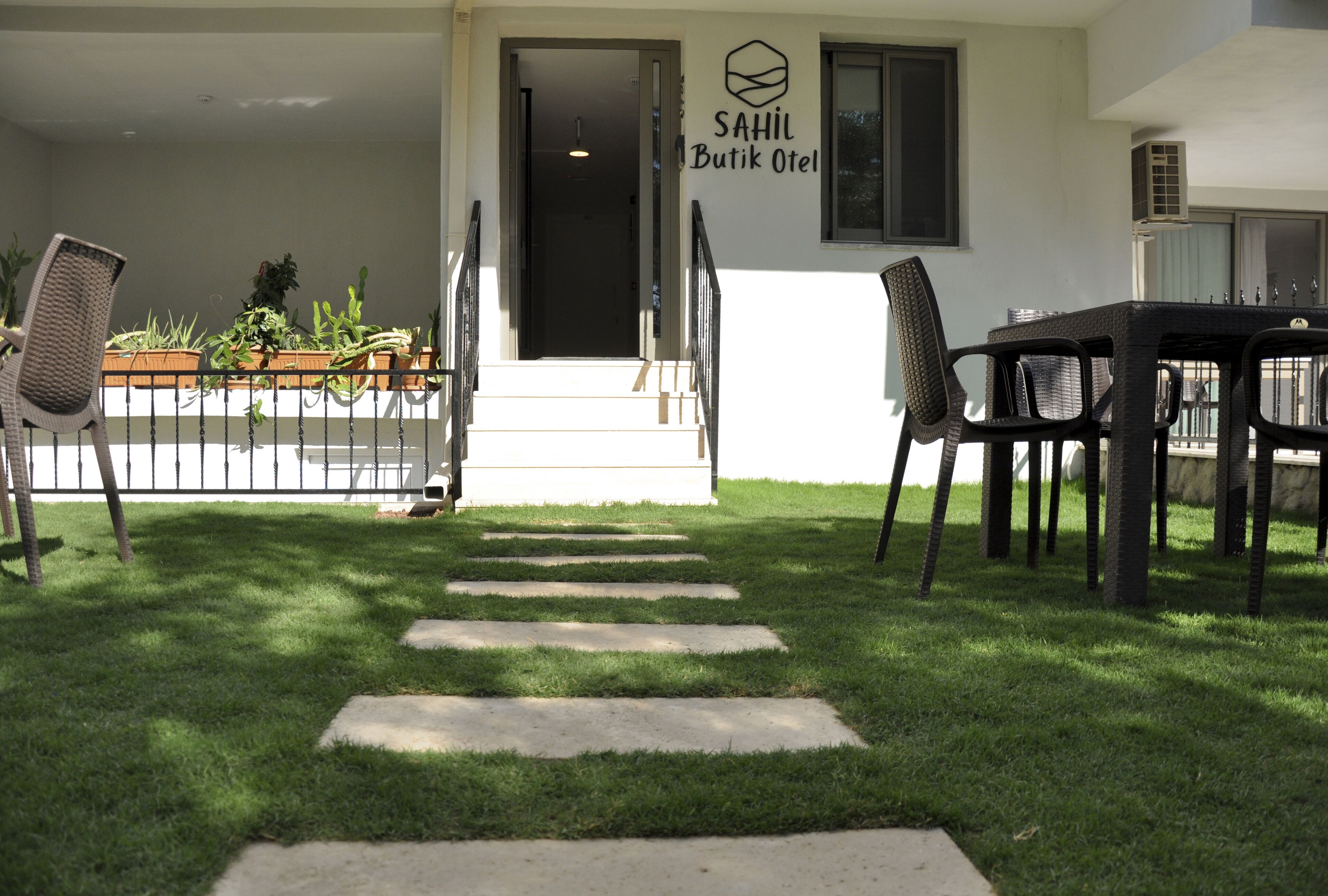 A hotel entrance with a staircase leading to the door, outdoor seating area with chairs and a table, and potted plants on the left.