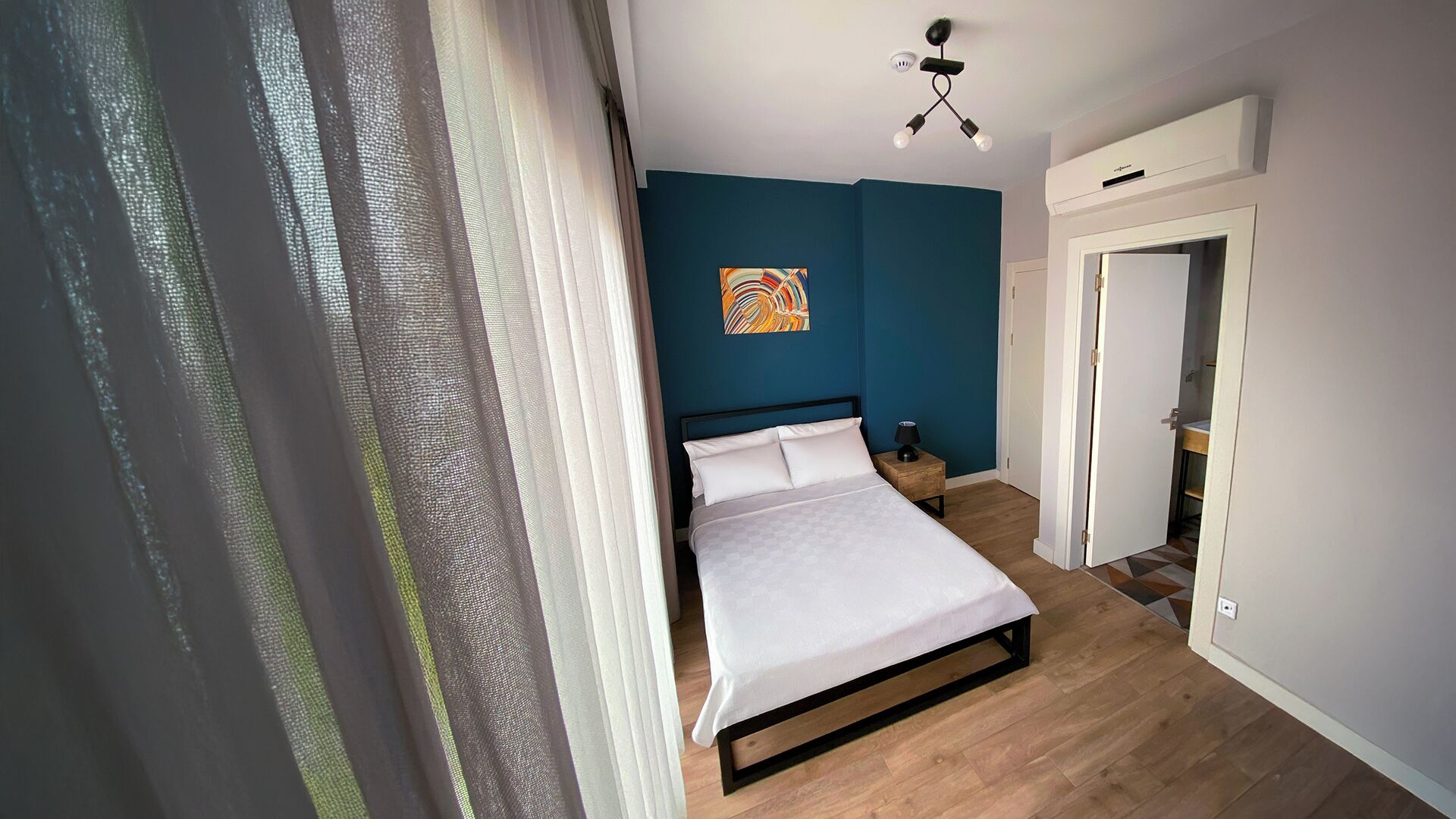 Een slaapkamer met een bed, nachtkastje, schilderij en deur naar een badkamer.