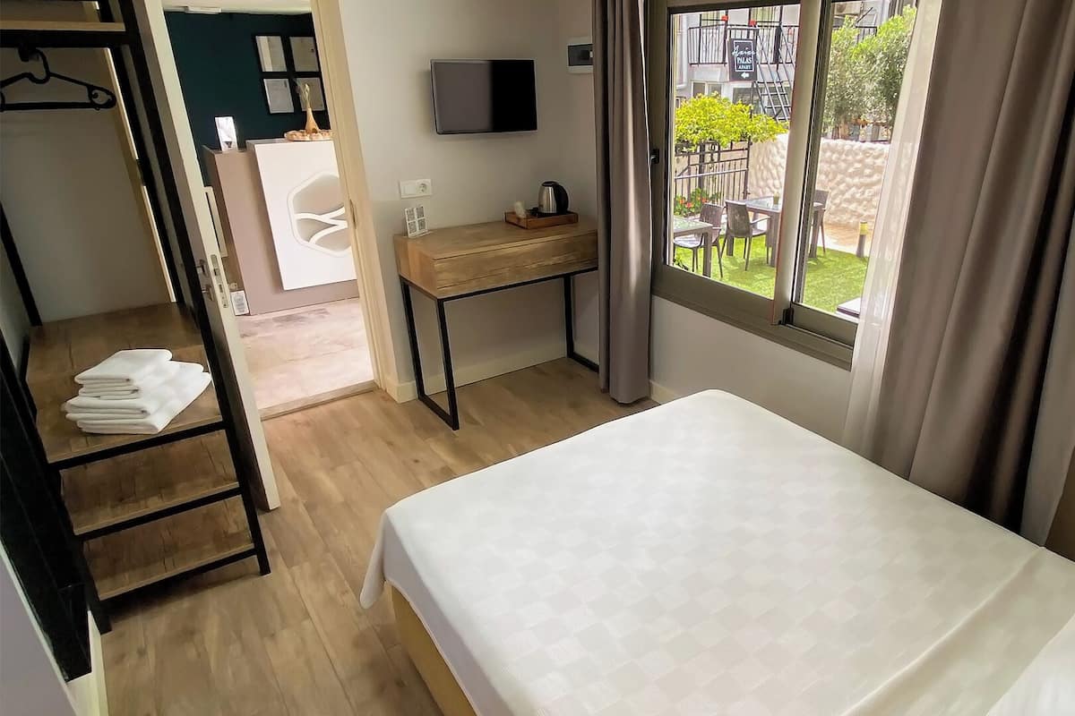 A hotel room with a bed, a desk, a TV, and a view of the outdoor area.