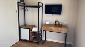 A compact room with a built-in wardrobe, a small refrigerator, a wooden desk with a flat-screen TV, and a kettle on the desk. - Sahil Otel (Cesme)