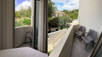 A balcony with a bed, two wicker chairs, and a view of greenery and buildings.