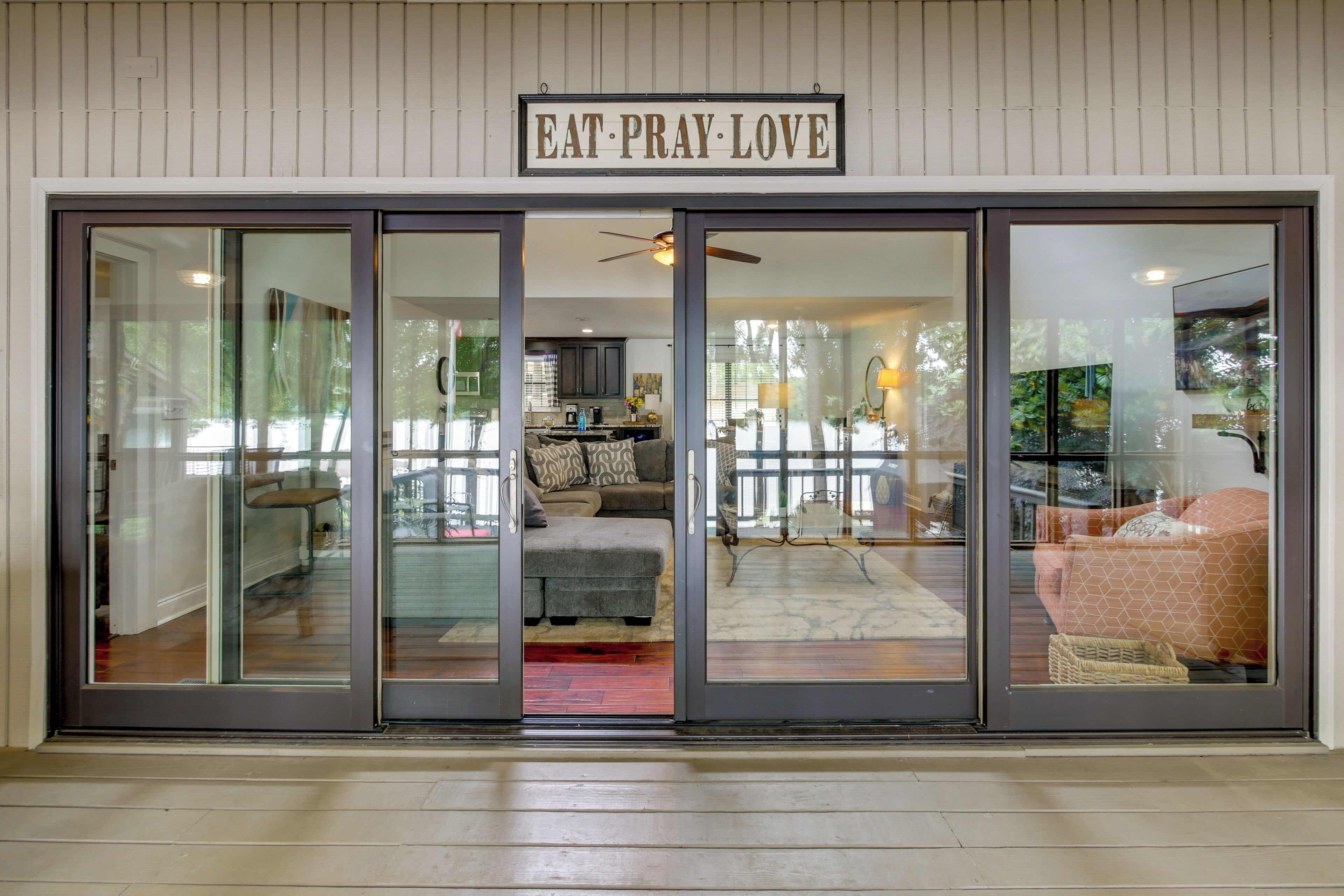 Une entrée moderne avec une porte en verre, un ventilateur de plafond et une enseigne sur laquelle on peut lire : « MANGE, PRIE, AIME ».