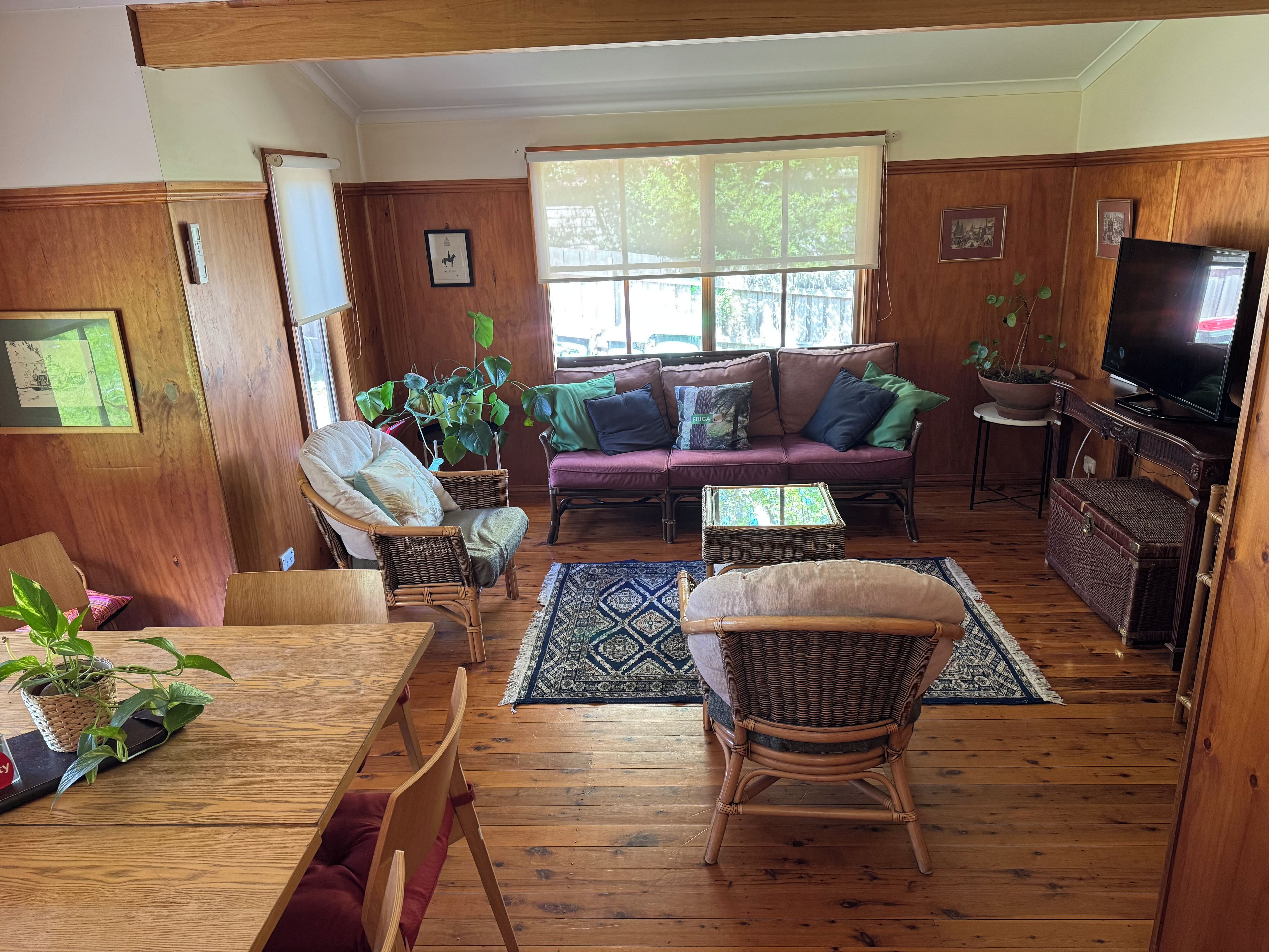 Una sala acogedora con piso de madera, un sofá, una mesa de comedor con sillas y un televisor.