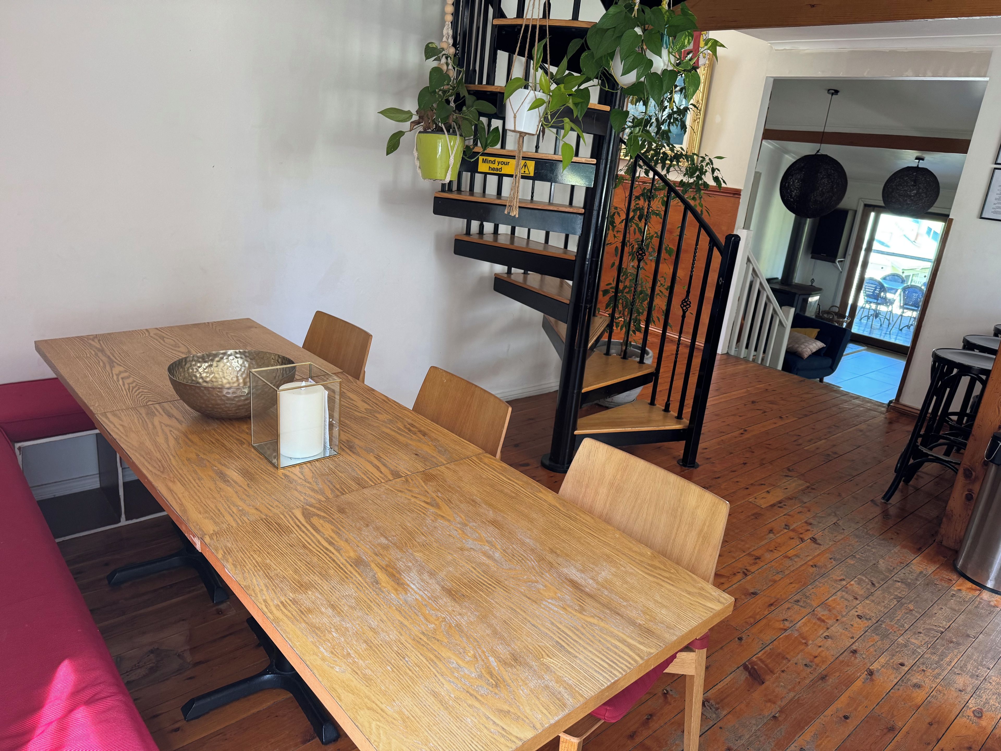 A dining area with a wooden table, chairs, a clear glass bowl, a white candle, and a potted plant.