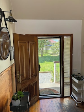 A wooden door leading to a covered outdoor area with a view of a fence and greenery. - Erica Escape – Where Humans Meet Nature (Erica)