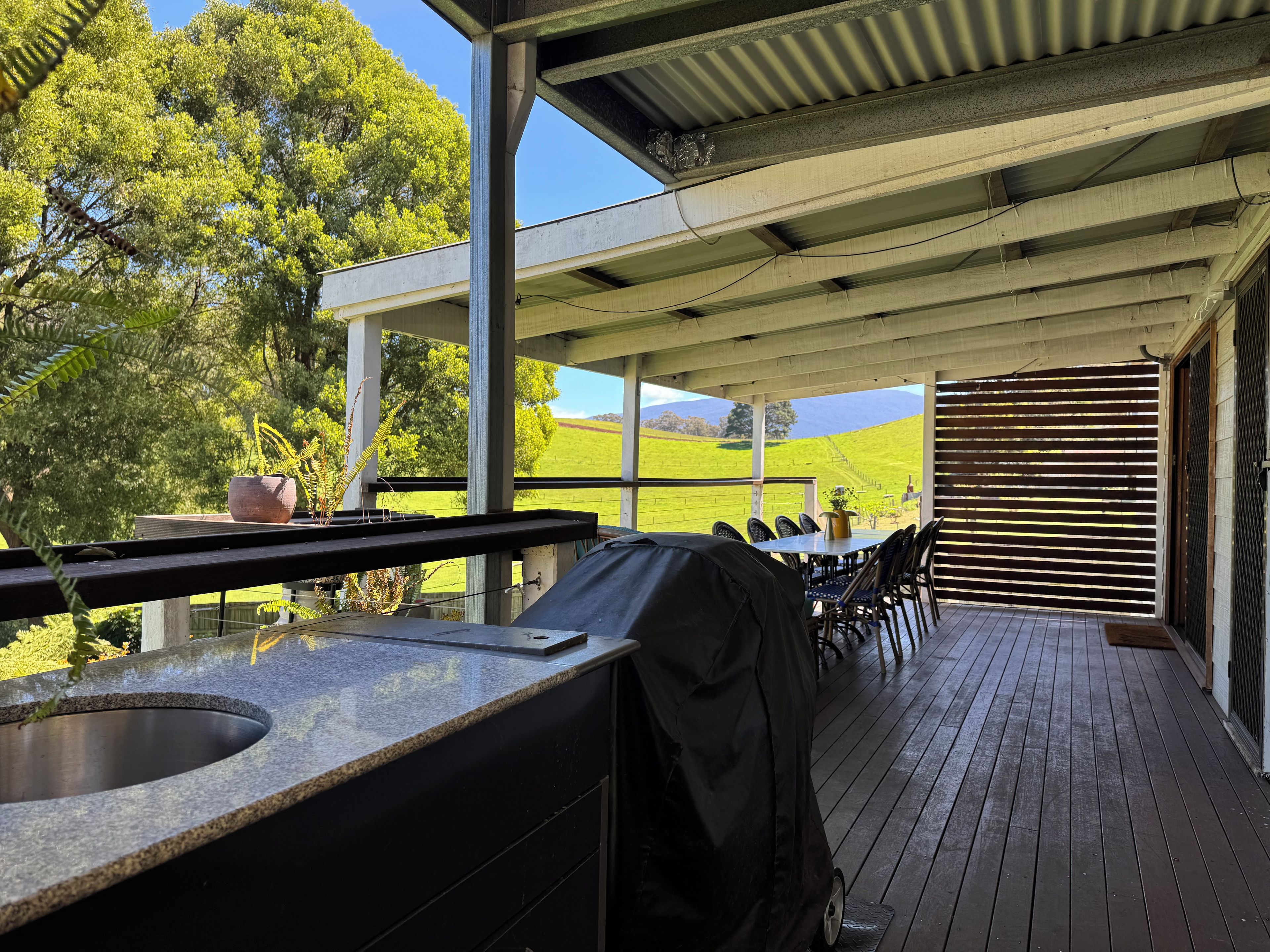 Une terrasse extérieure équipée d’un barbecue, d’un espace salon et offrant une vue sur un champ verdoyant.