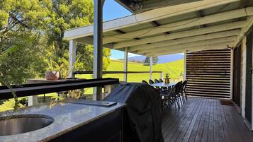Une terrasse extérieure équipée d’un barbecue, d’un espace salon et offrant une vue sur un champ verdoyant.