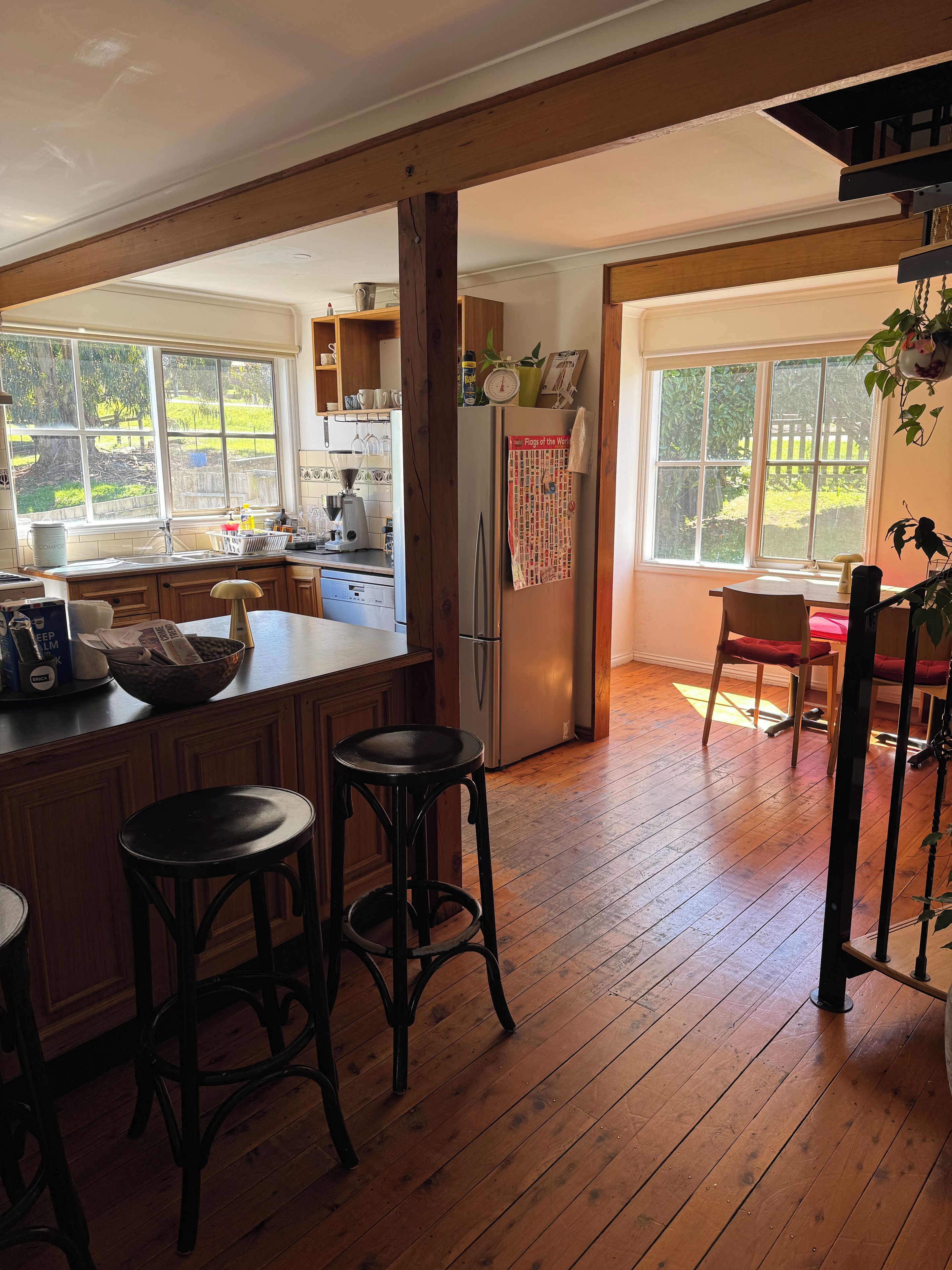 A kitchen with wooden floors, a refrigerator, and a window overlooking a yard.