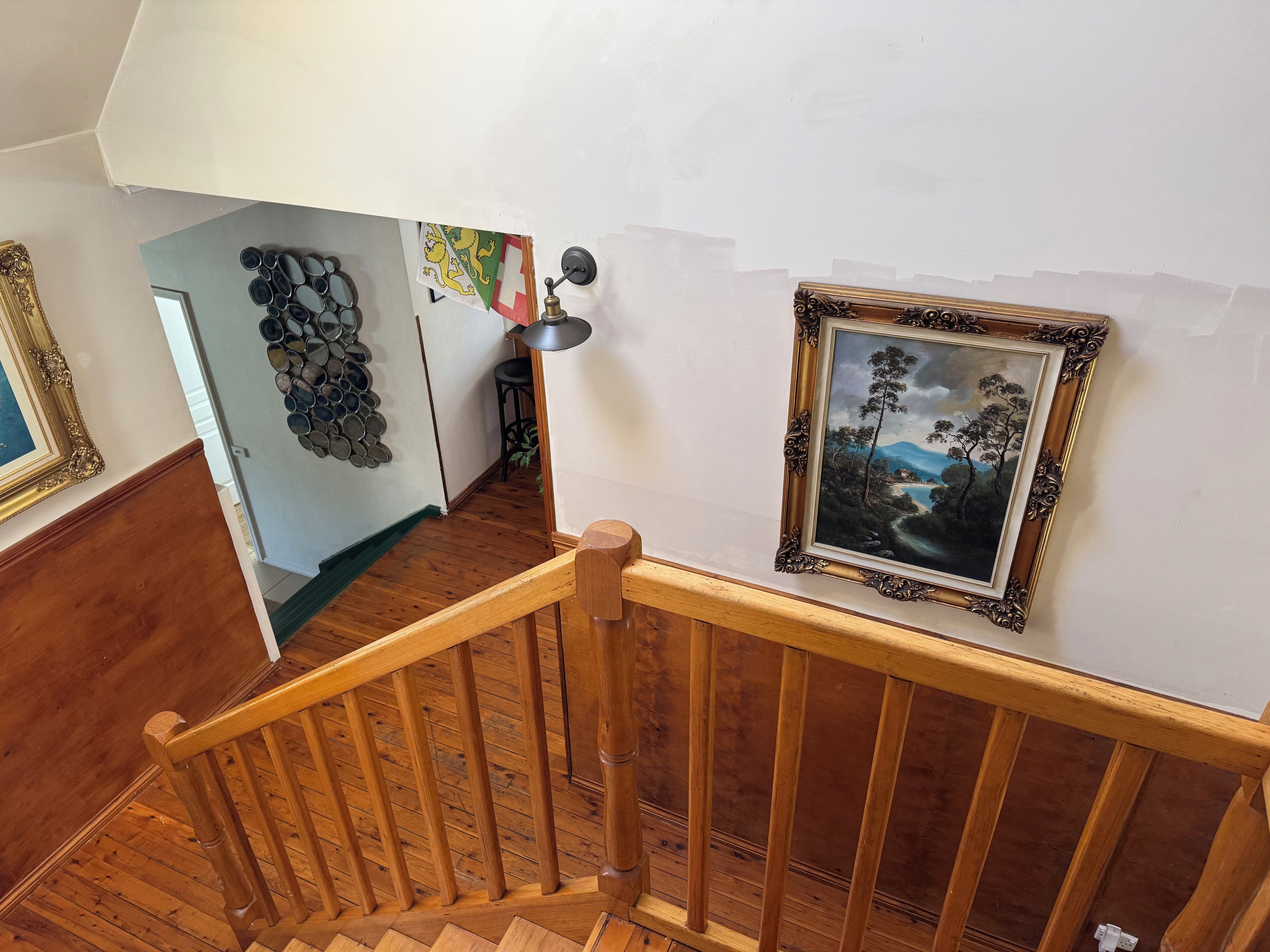 Eine Holztreppe mit Geländer, ein gerahmtes Gemälde an der Wand und ein dekorativer Wandbehang.