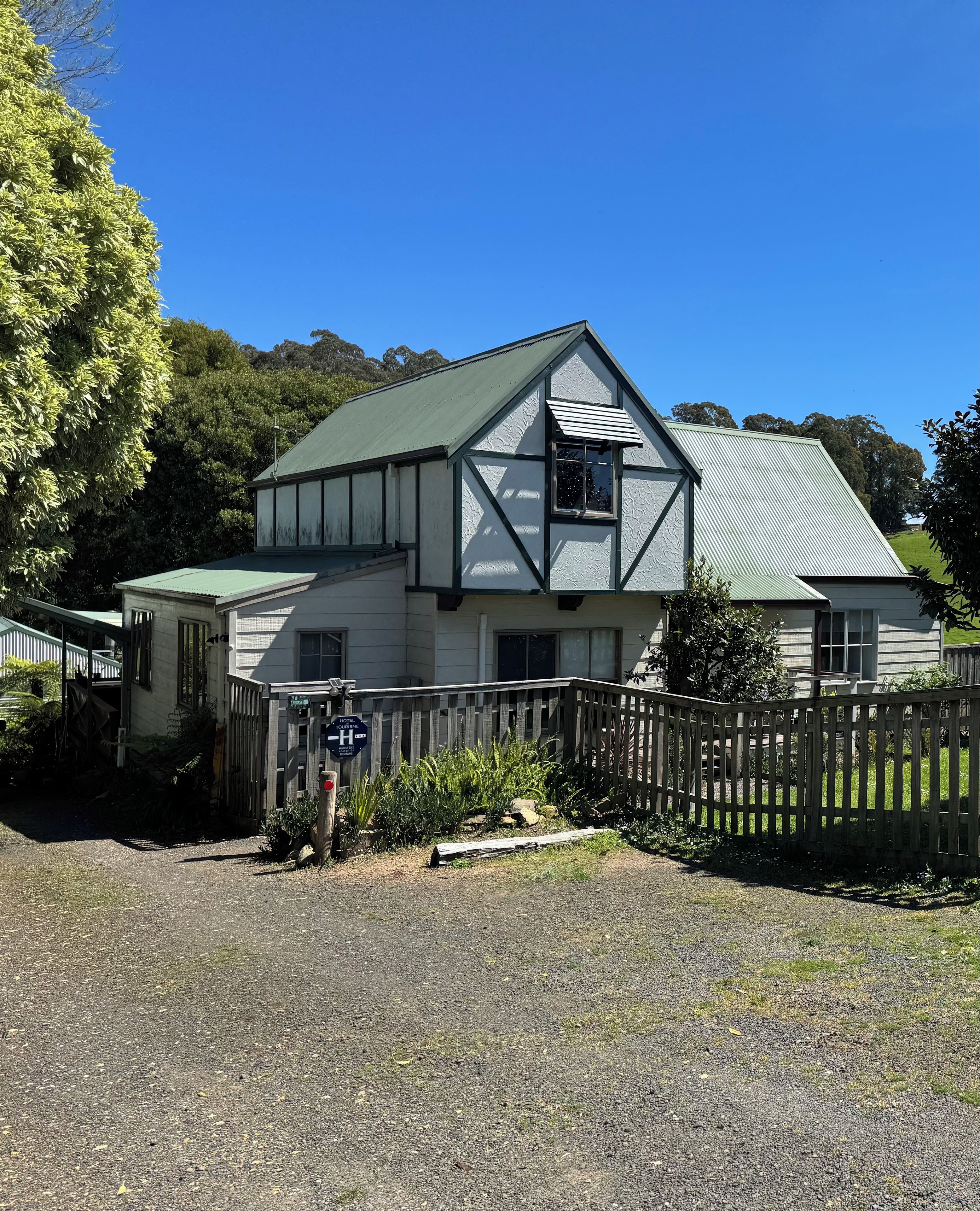 A two-story building with a prominent gable roof, a visible balcony, and a gravel driveway.