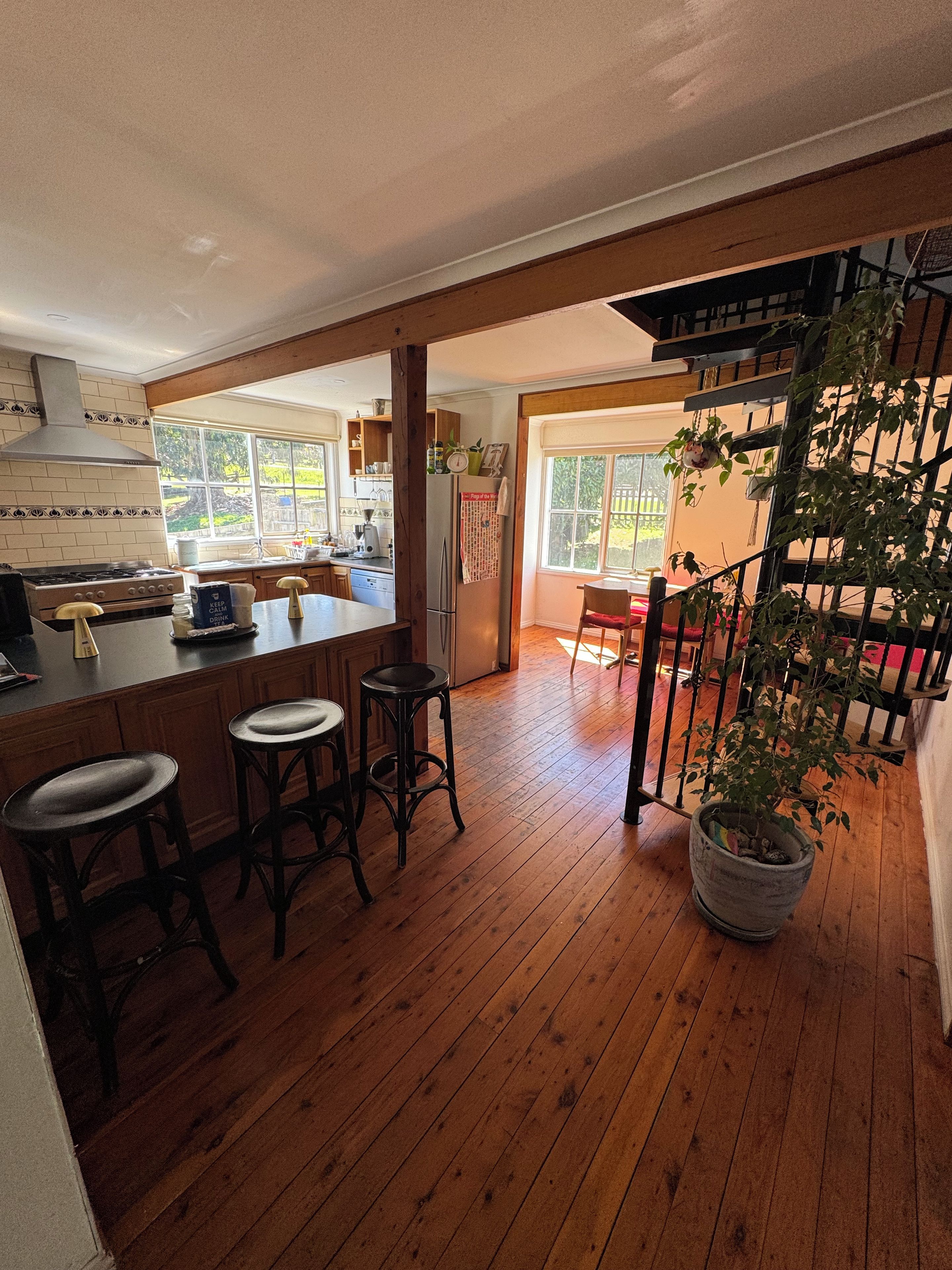 Une cuisine avec un plancher en bois, un îlot central doté de tabourets, un réfrigérateur et une fenêtre donnant sur un jardin.