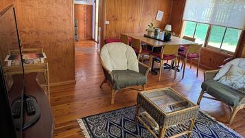 A room with a wooden floor, a dining table with chairs, a television, and a patterned rug.