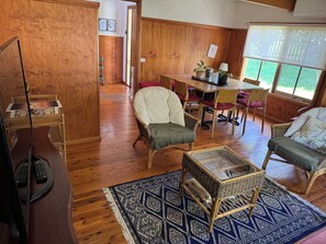 Une pièce avec un plancher en bois, une table à manger avec des chaises, un téléviseur et un tapis à motifs.