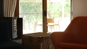 A room with a wicker trunk, a vintage radio, and a chair by a sliding glass door leading to an outdoor area with chairs. - "Experience the ultimate retreat surrounded by the untouched beauty of nature.  (Erica)