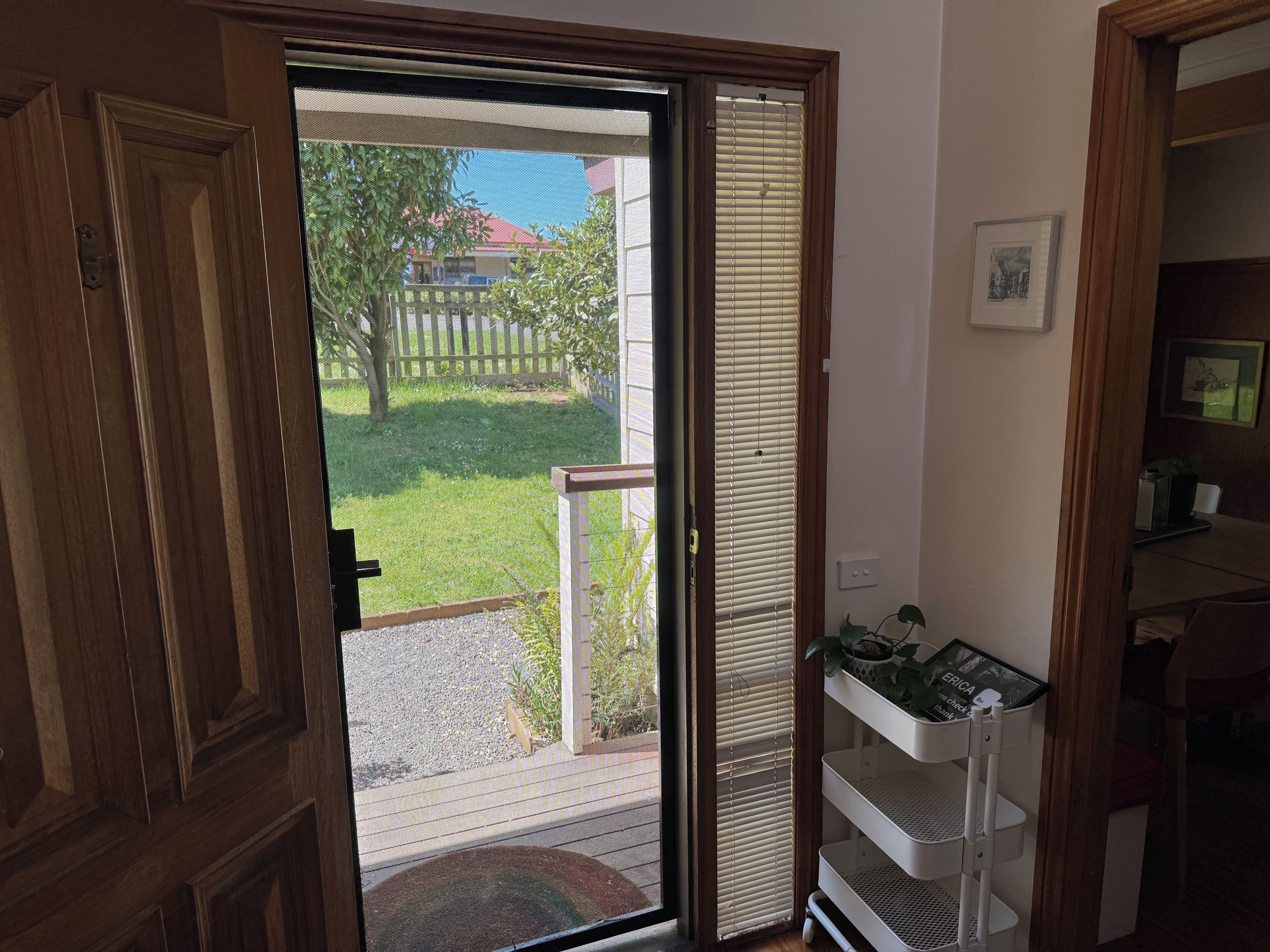 Ein Zimmer mit einer Schiebetür, die auf einen Balkon mit Blick auf einen umzäunten Garten und einen Baum führt.