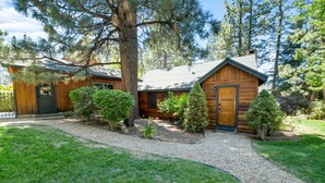 A log cabin with a gravel driveway, surrounded by trees and a well-maintained lawn.