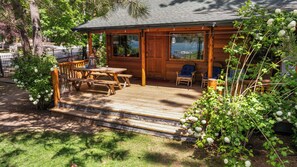 A cabin with a wooden deck, picnic table, and two blue chairs. - Stillwater Cove Lakefront - Lakefront, Boat Dock, Pet Friendly, Fenced Yard (Big Bear Lake)