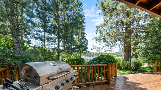A barbecue grill on a wooden deck with a view of trees and a lake.