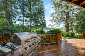 Una parrilla de barbacoa en una terraza de madera, con vista a árboles y un lago.