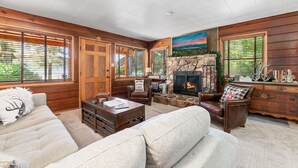 A cozy living room with a fireplace, wooden walls, and large windows.