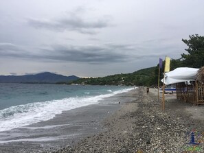 A beach with pebbles, a few people, and a mountain in the background. - Cerca Parola Beach Resort by Cocotel (Lobo)